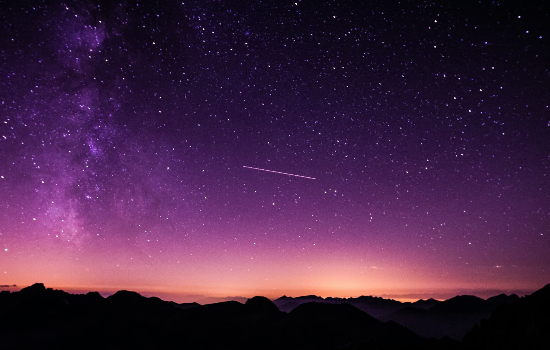 A star-filled night sky above a silhouetted mountain ridge
