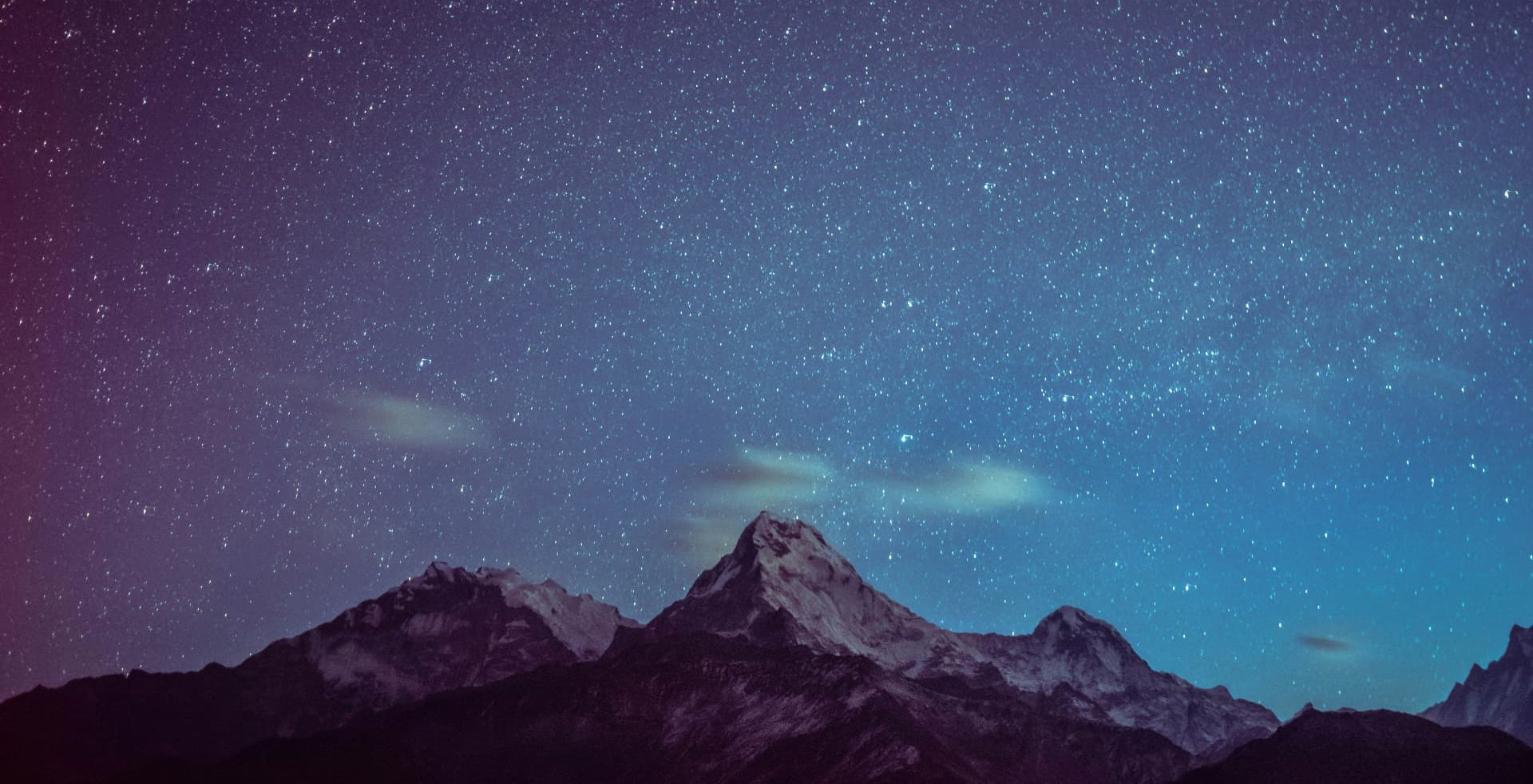 A star-filled night sky above snow-lit mountain peaks